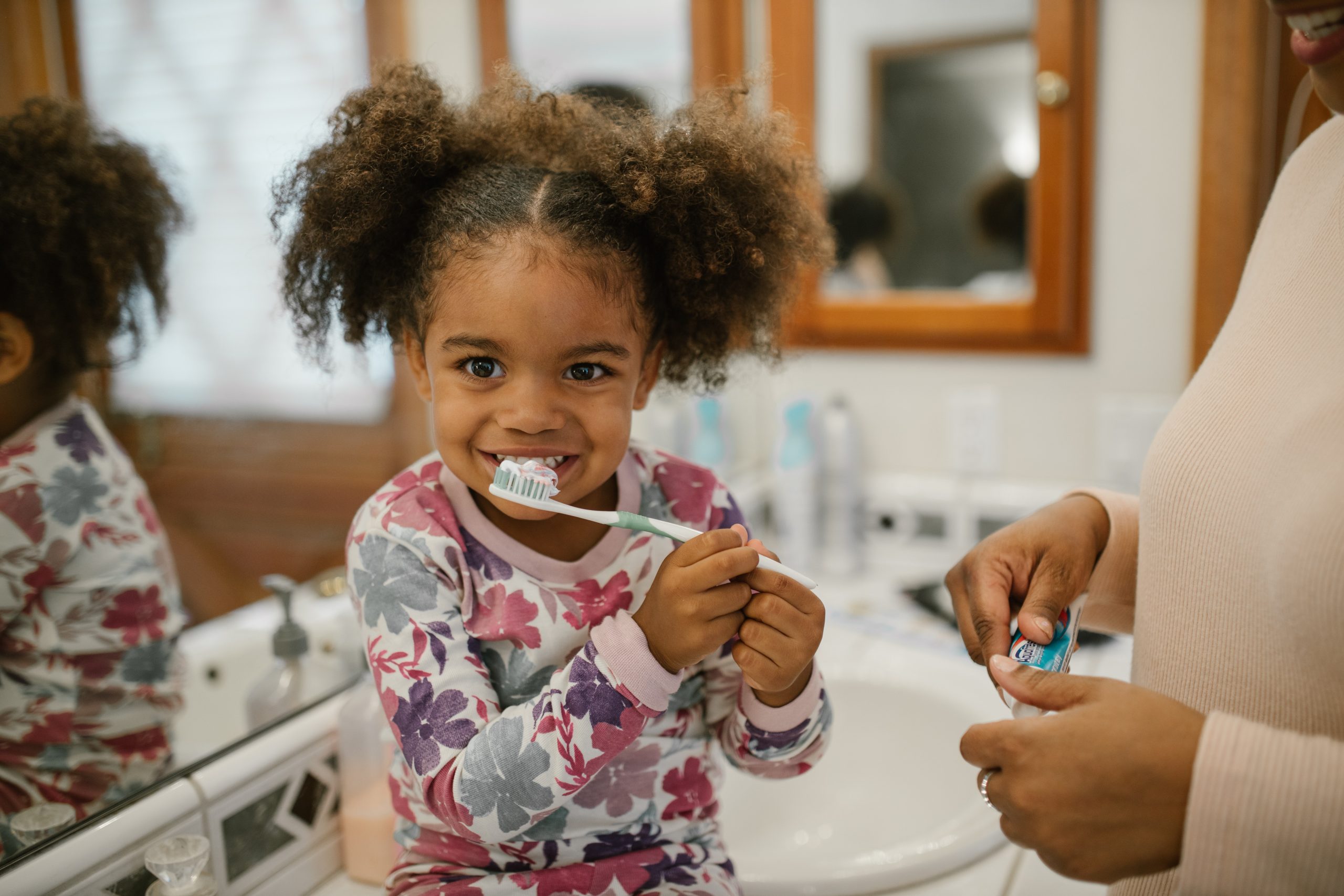 Smiling child brushing teeth with parent assistance at home